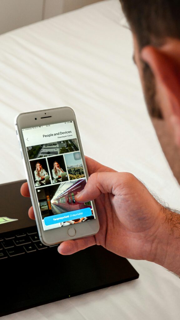 Close-up of a man browsing photos on a smartphone, with a laptop in the background.